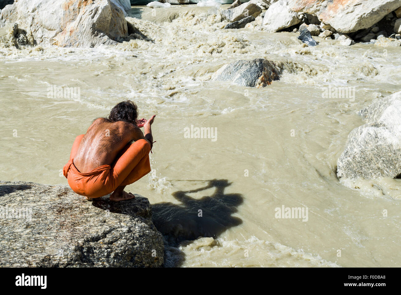 A Sadhu, holy man, is sitting and praying on a rock at Gaumukh, the main source of the holy river Ganges, Gangotri, Uttarakhand Stock Photo
