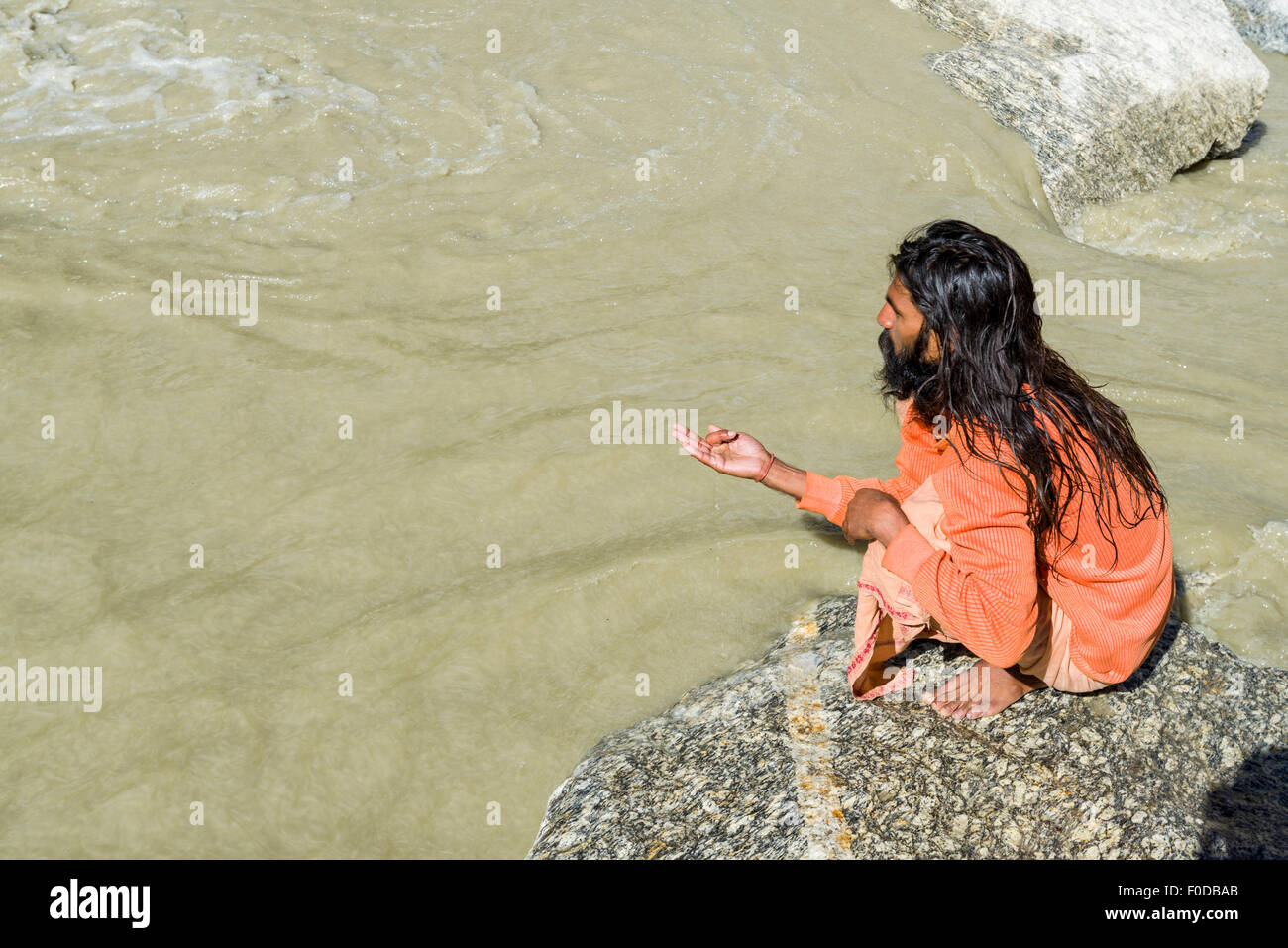 A Sadhu, holy man, is sitting and praying on a rock at Gaumukh, the main source of the holy river Ganges, Gangotri, Uttarakhand Stock Photo