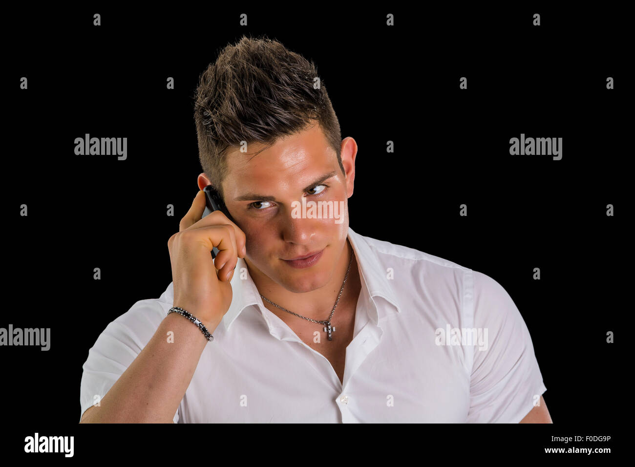 Handsome hunky young man talking on cell phone, isolated on black. Looking to a side Stock Photo
