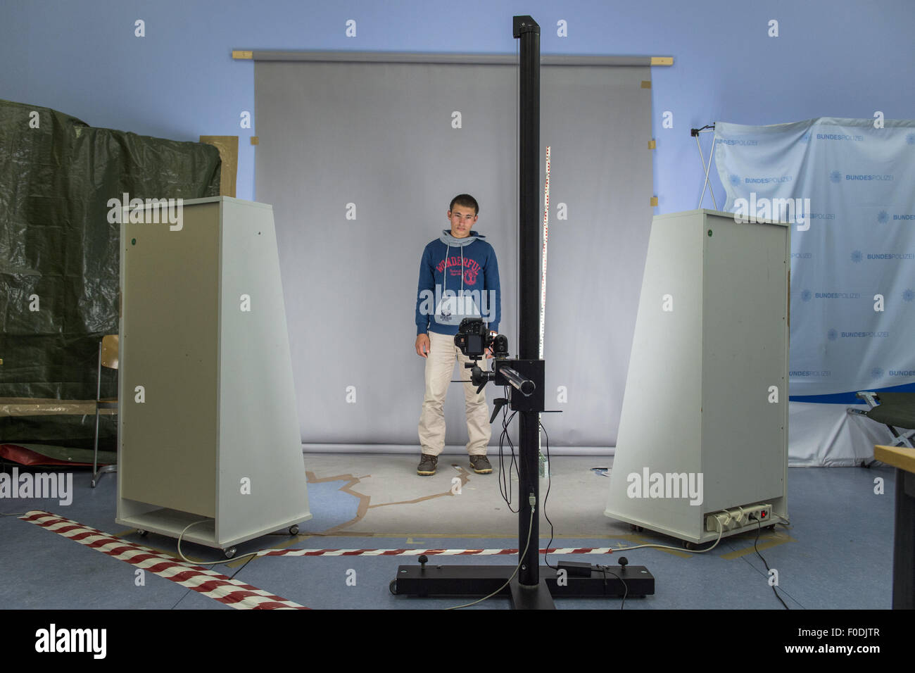 Illuminated by spotlights is 16 year old refugee Kahlil from Afghanistan in an improvised police station at Frankfurt main station, Germany, 5 August 2015. Hasan is being photographed as per the digital identification procedures in place. Alluding to the wall color to officials call the room "Blue Lagoon". The illiterate asylum seeker was abandoned by smugglers after months spent fleeing without family members. Photo: BORRIS ROESSLER/dpa Stock Photo