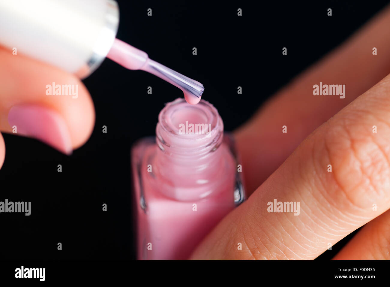 Open pink bottle of nail polish in manicured woman palms on black