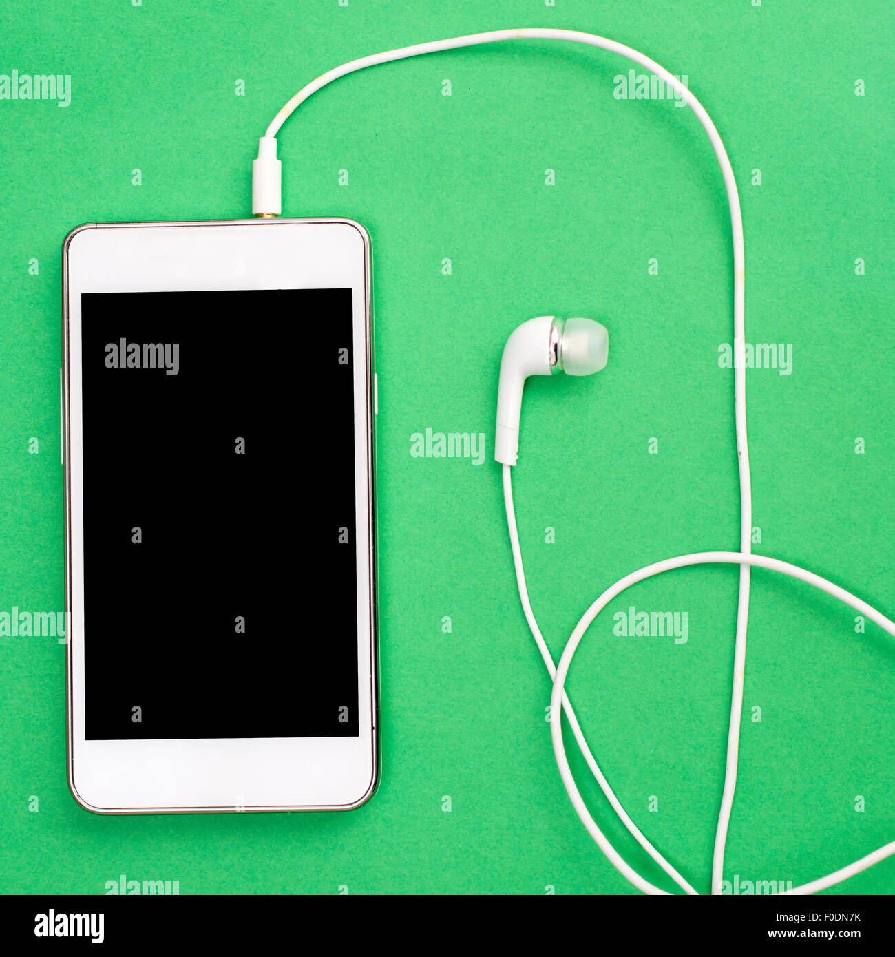 White smart phone with earphones and isolated screen on green, from above Stock Photo