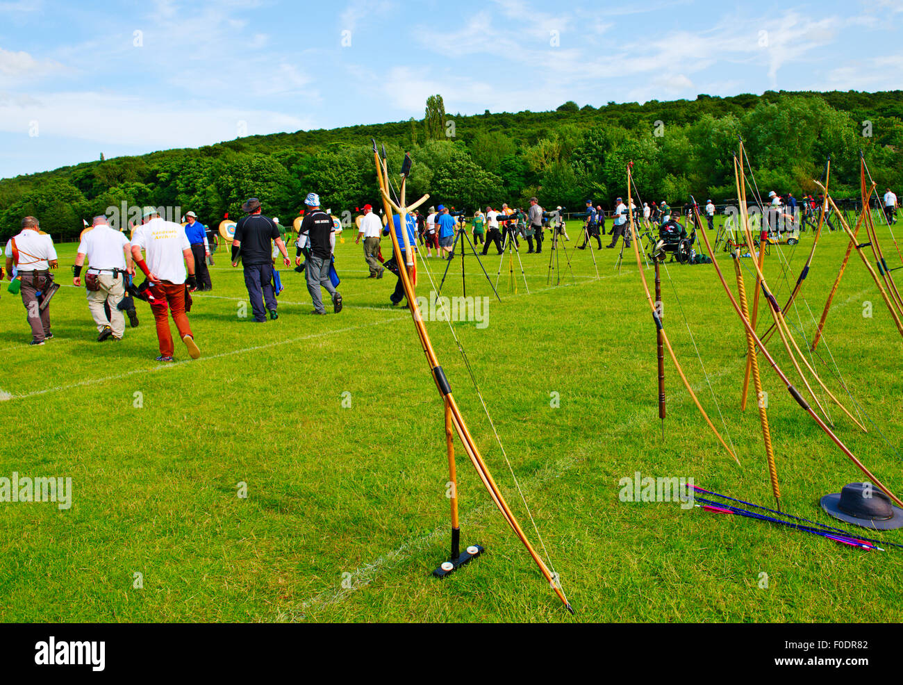 Archery competition, row of traditional longbows lined up behind shooting line with archers walking to targets to retrieve arrow Stock Photo
