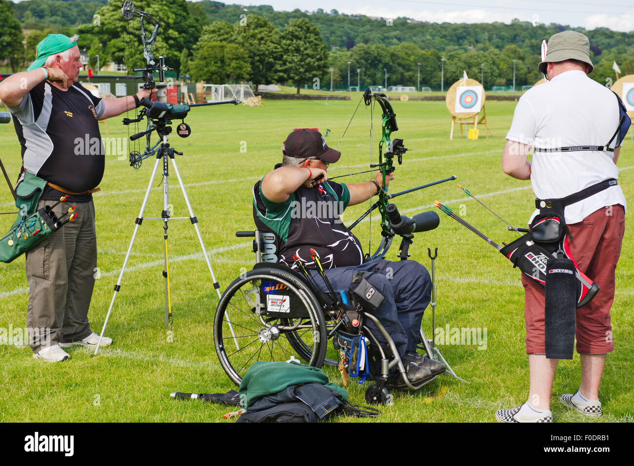Two male archers in line shooting modern compound style bows in competition, one in wheelchair, West Yorkshire, England Stock Photo