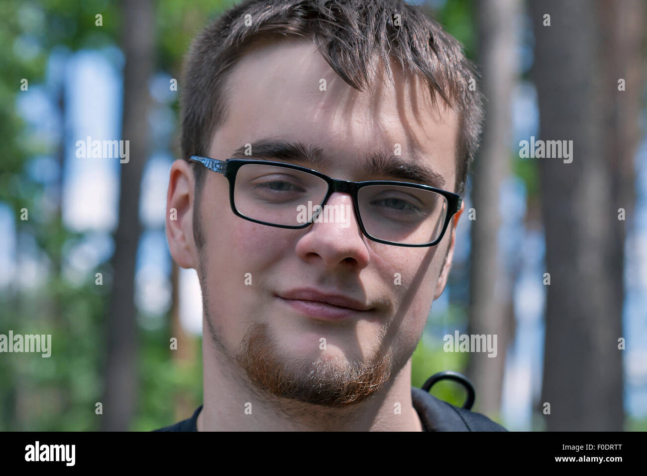 portrait of caucasian young man in glasses with a beard and a backpack on the background of the forest Stock Photo