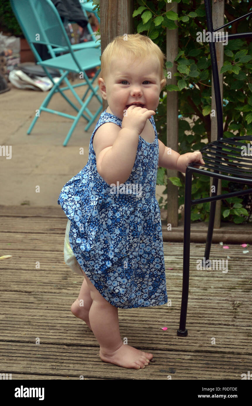 A ten month old baby standing supporting herself with a garden chair