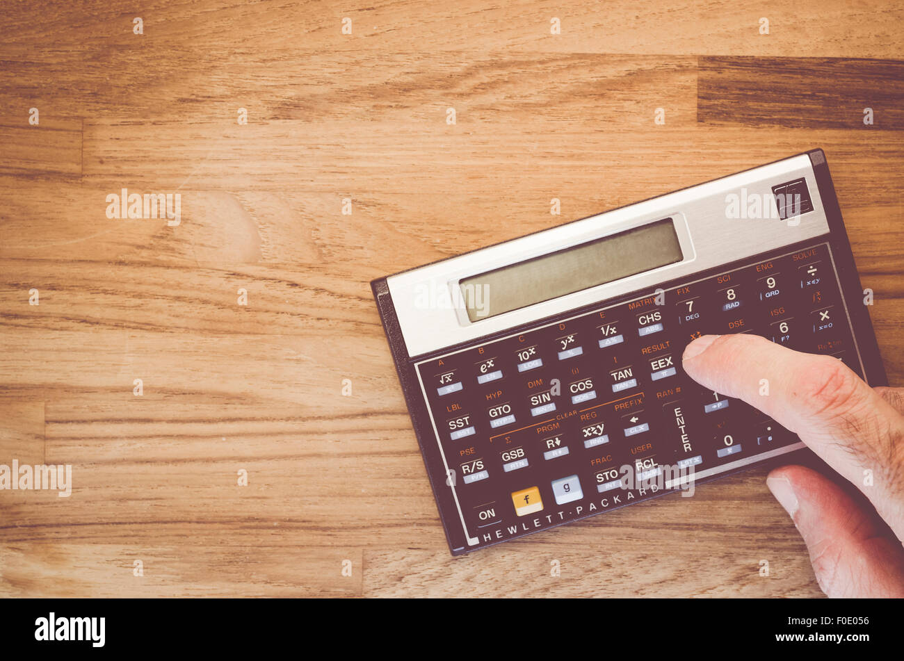 HP15C programmable scientific calculator with finger on a natural wood