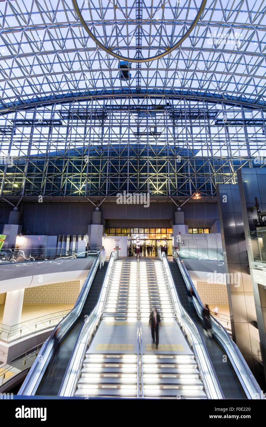 Japan, Kanazawa. JR station, interior of the outside glass atrium, Motenashi (Welcome) Dome, with escalators to lower level shopping area. Night time. Stock Photo