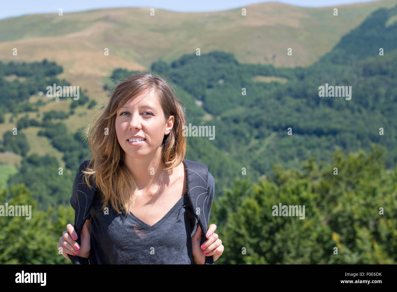 Portrait of happy girl hiker with backpack in the mountains surrounded by green vegetation. Hiking trip Stock Photo