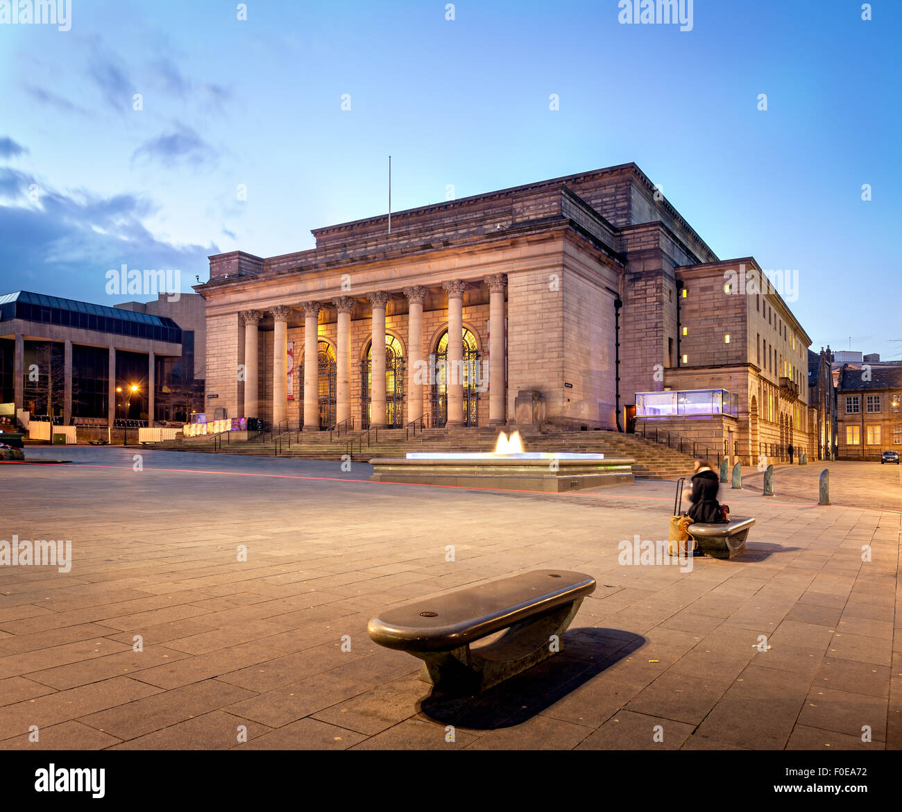 Sheffield city hall building illuminated at night. A woman waiting alone on bench with her luggage. Stock Photo