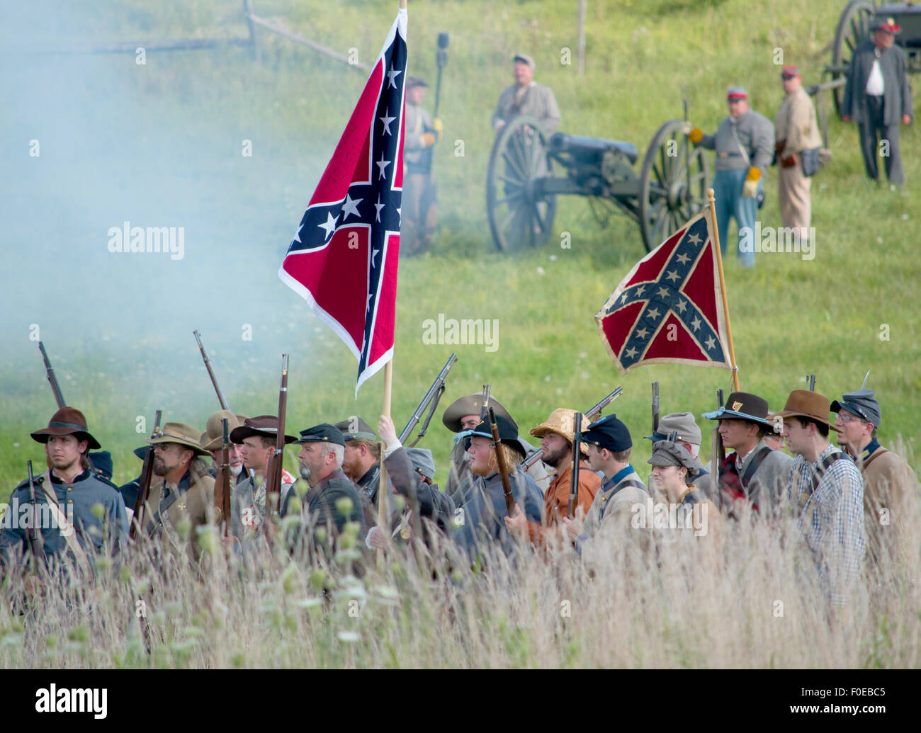 Gettysburg Confederate Army marching through fields with flags, cannons in background. Stock Photo