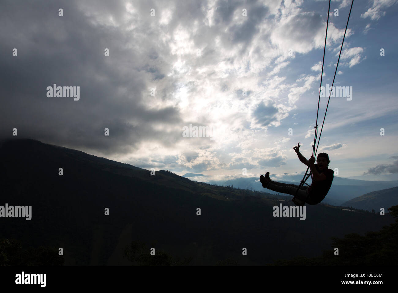 Silhouette of happy young man on a swing with a fantastic mountain view at the Casa del Arbol, Ecuador Stock Photo