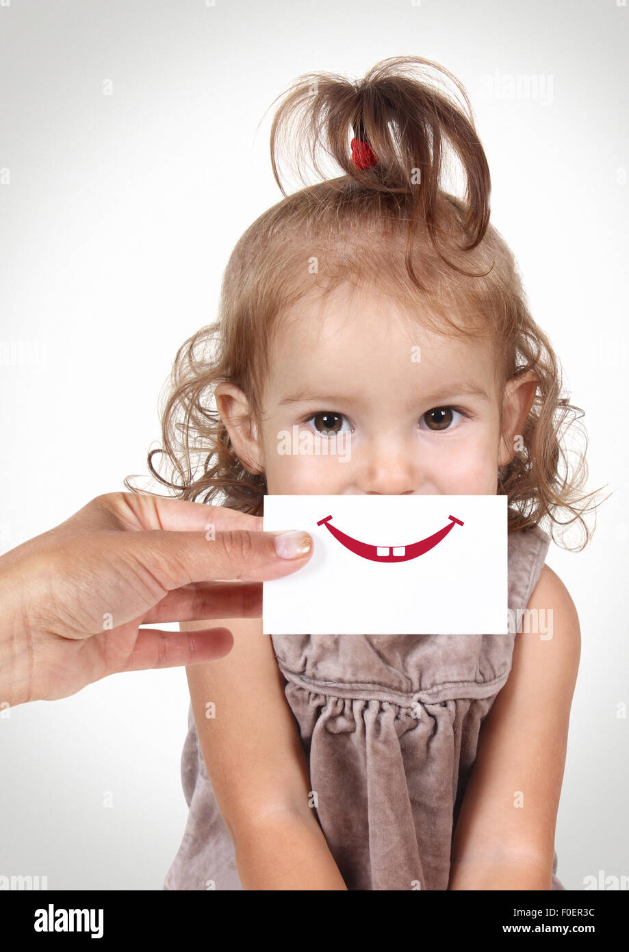 Happy joyful baby girl hiding her face by hand with smile and teeth drawn on paper Stock Photo