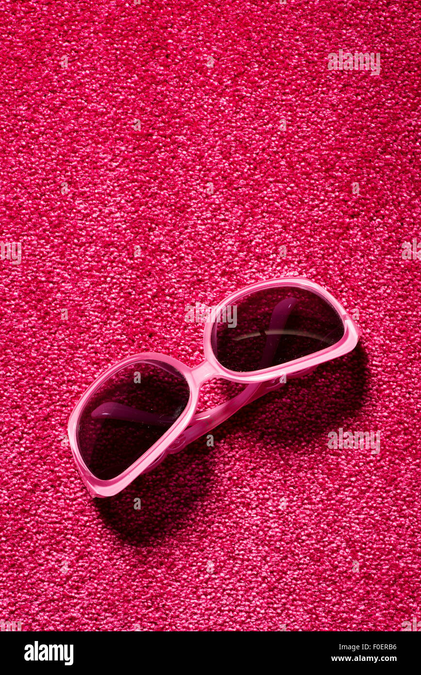 Still life of pink plastic sunglasses lying on red carpet. Copy space above the glasses. Stock Photo