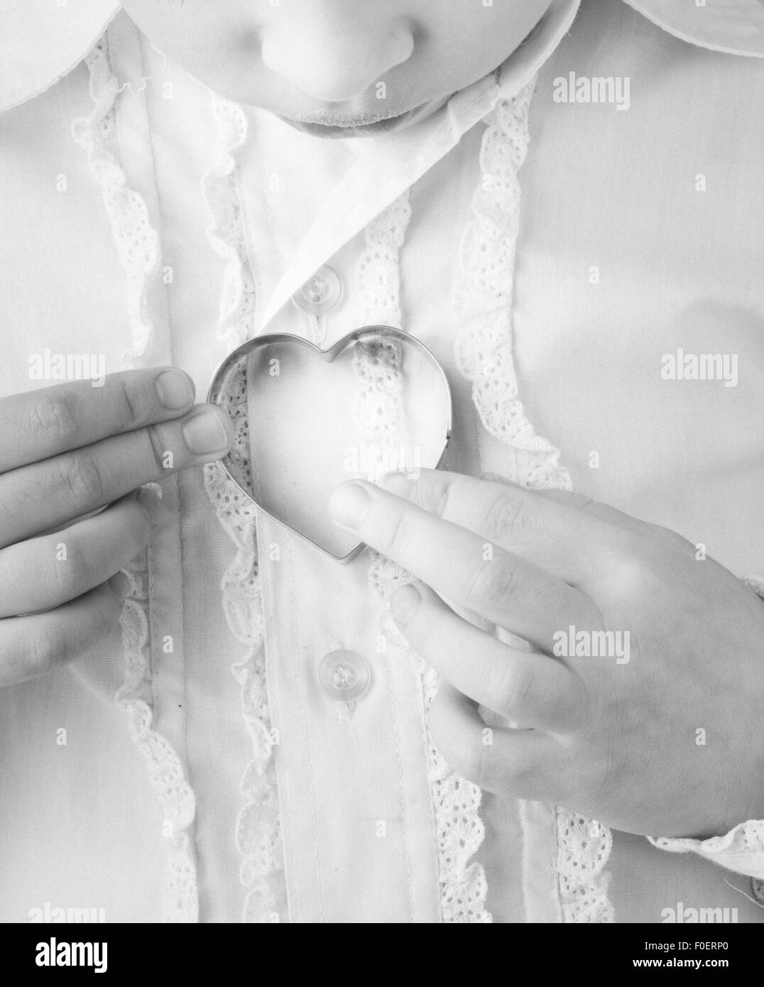 Little girl holding heart shaped cookie cutter in her hands. Conceptual image of childhood, love and affection. Stock Photo