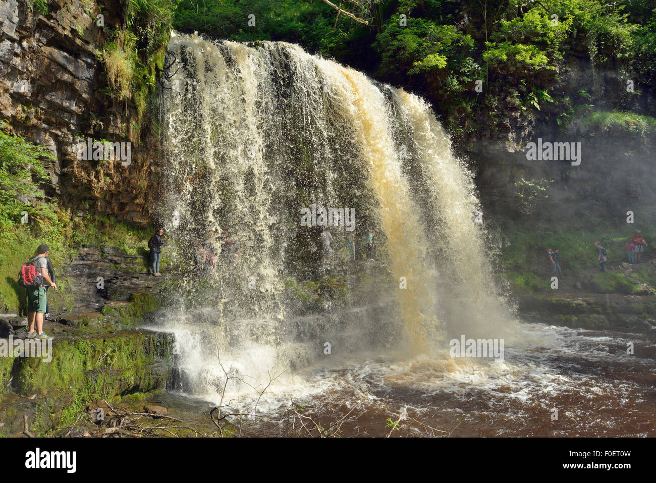 People walking behind Sgwd yr Eira Waterfall; Afon Hepste River Brecon Beacons, Wales Stock Photo