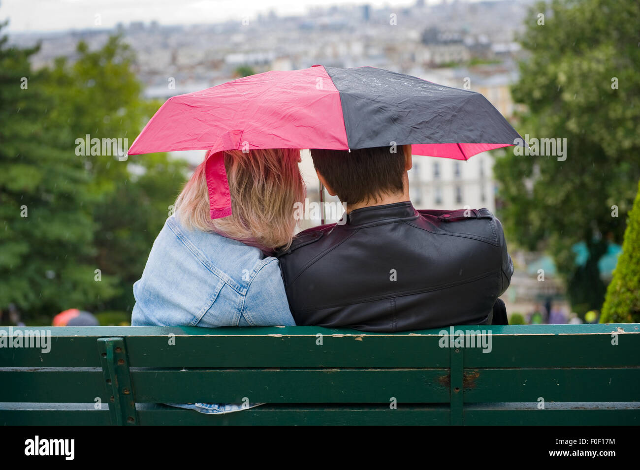 PARIS, FRANCE - JULY 27, 2015: A couple is sitting on a bench under an umbrella during a rainy day in Mont Matre in Paris in Fra Stock Photo