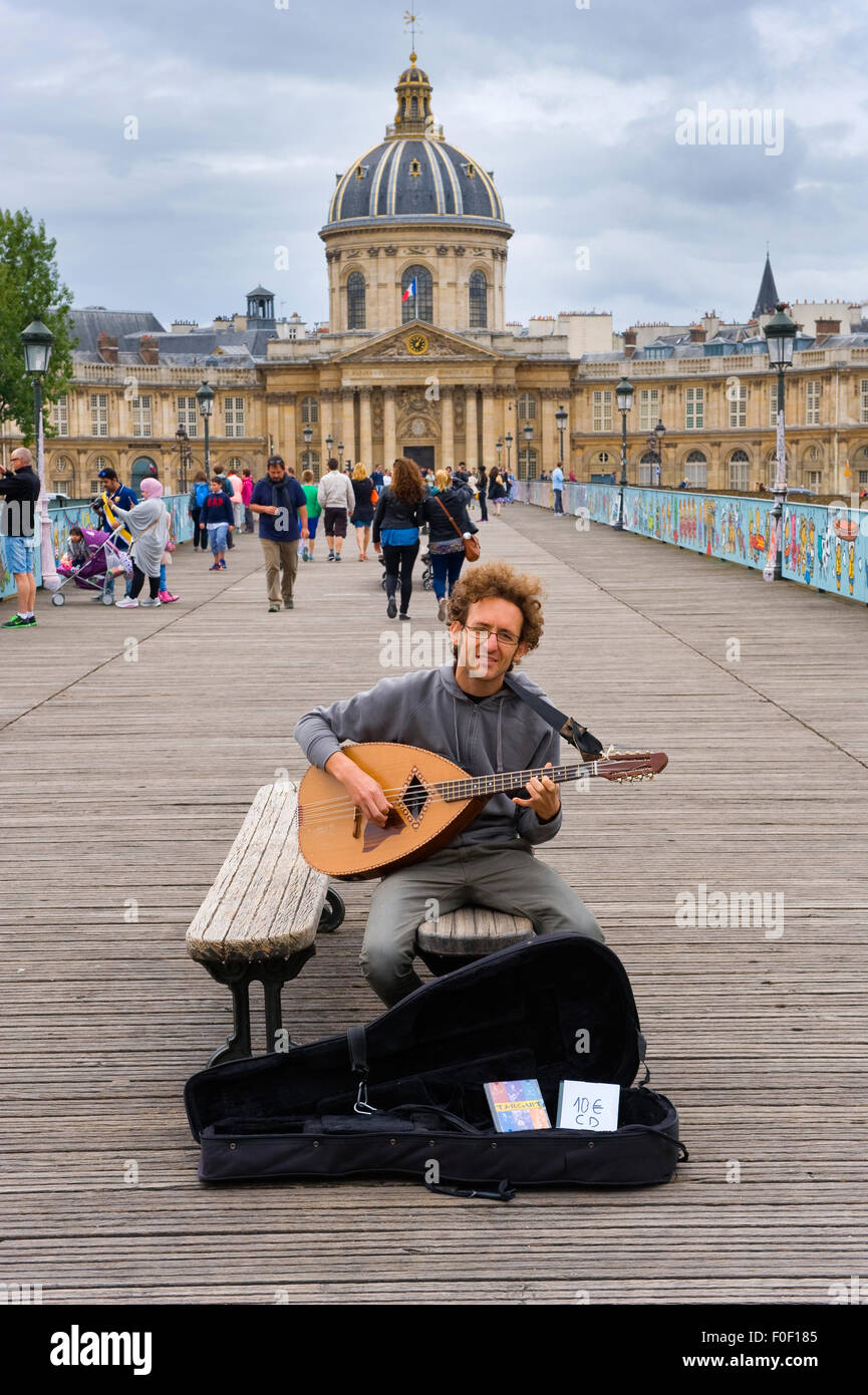 PARIS, FRANCE - JULY 27, 2015: A musician is playing guitar on 'Love Locks bridge' with the Academy of Fine Arts on the backgrou Stock Photo