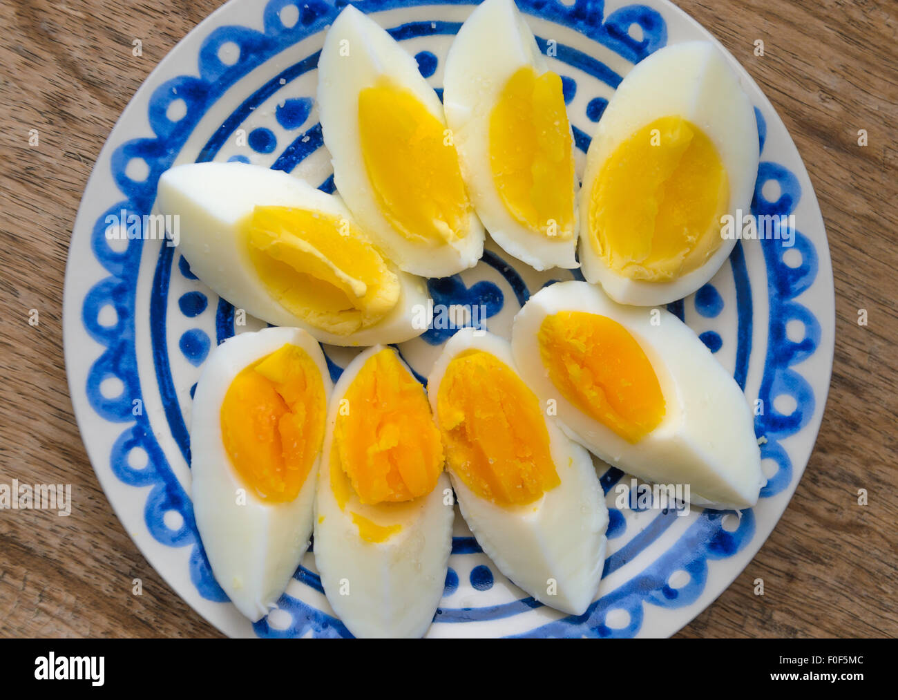 Two colors yolk, sliced hard boiled eggs in a blue decorated plate on wooden kitchen table. Stock Photo