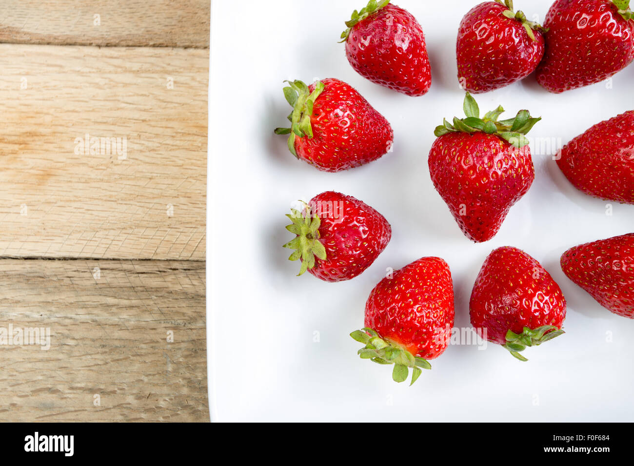 Arrangement of red strawberries on white dish with rustic wood ...