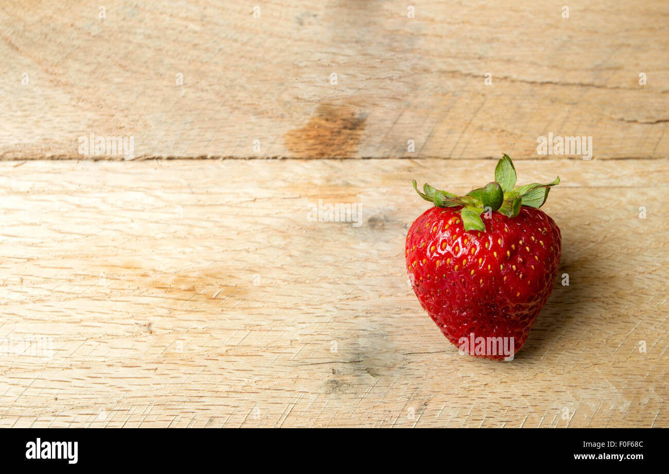 One organic strawberry on a rustic wood background Stock Photo - Alamy