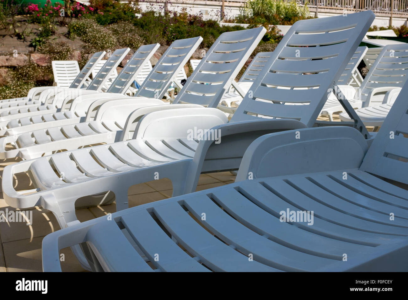 Empty sunloungers by the side of a swimming pool in a holiday complex Stock Photo