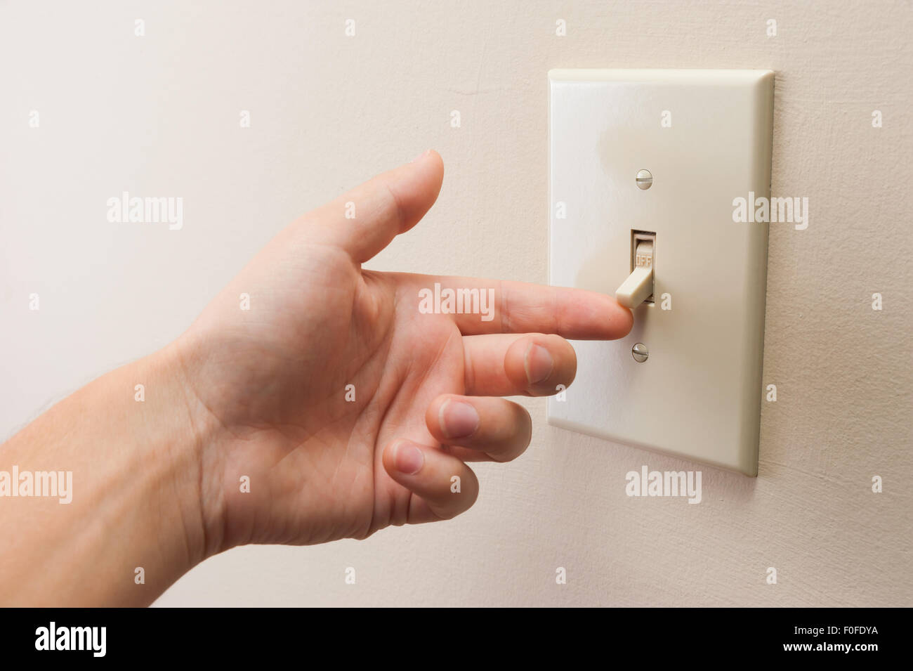 Hand turning wall light switch off. color image in horizontal