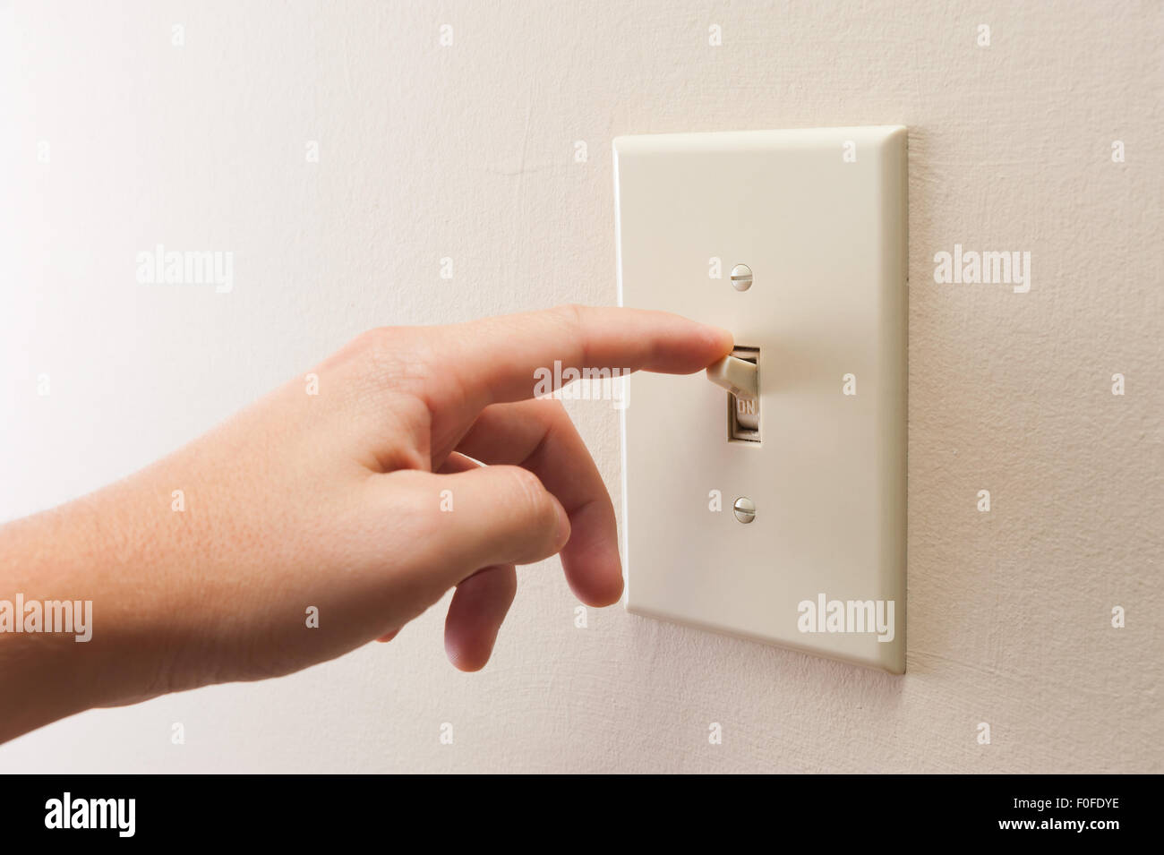 Hand turning wall light switch off. color image in horizontal