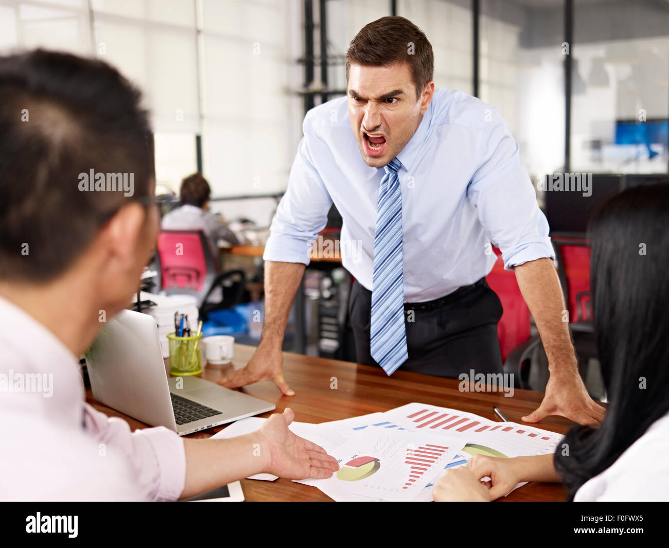 bad-tempered caucasian business executive yelling at two asian subordinates in office. Stock Photo