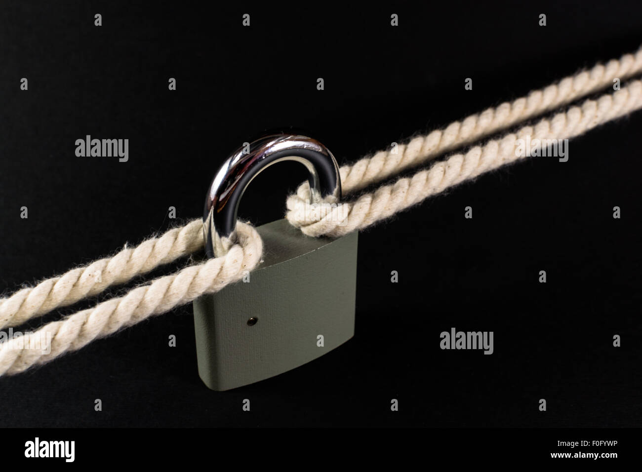 Locked padlock secures two separate ropes together under tension Stock