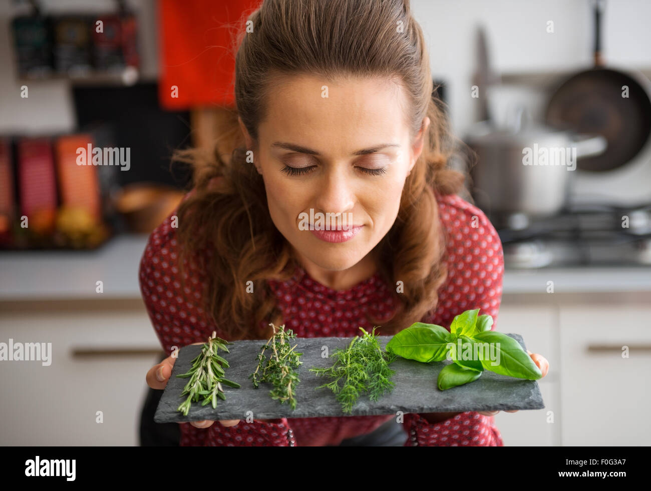 Oh, the heady smell of fresh herbs, conjuring up dreams of all kinds of recipes... A woman, smelling deeply, and closing her eyes in pleasure, leans over a slate showing a few sprigs of fresh herbs. Stock Photo
