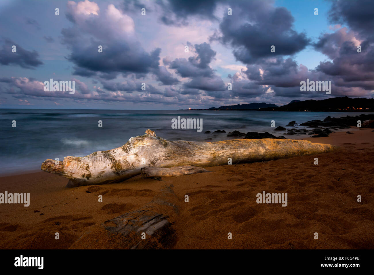 A log on a beach is Hawaii is painted with light at nighttime during a long shutter speed, creating a surreal, peaceful ambiance Stock Photo