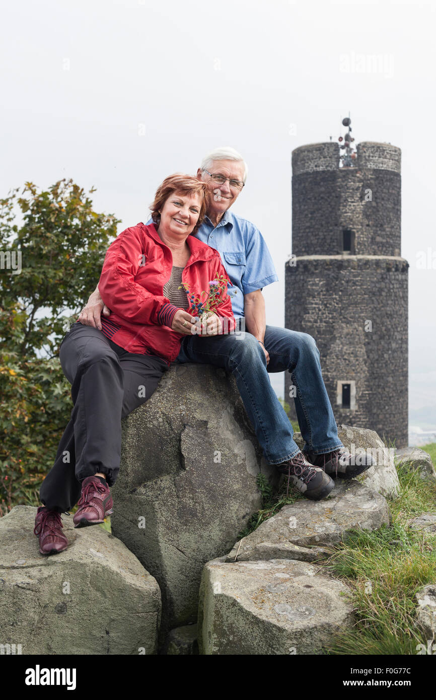 Portrait of happy senior couple resting on the rocks next to the ruins of Hazmburk castle in the Czech Republic. Stock Photo