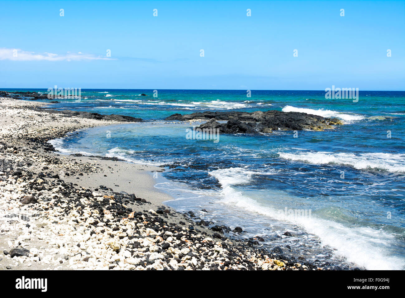 A beautiful black and white gravel beach with clear blue water on a remote beach in Kona Hawaii. Stock Photo