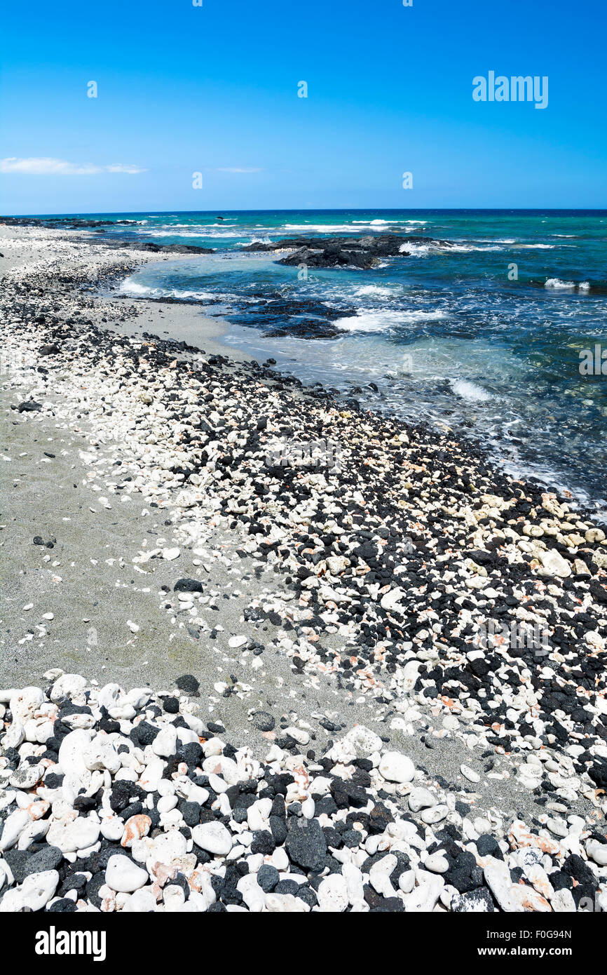 A beautiful black and white gravel beach with clear blue water on a remote beach in Kona Hawaii. Stock Photo