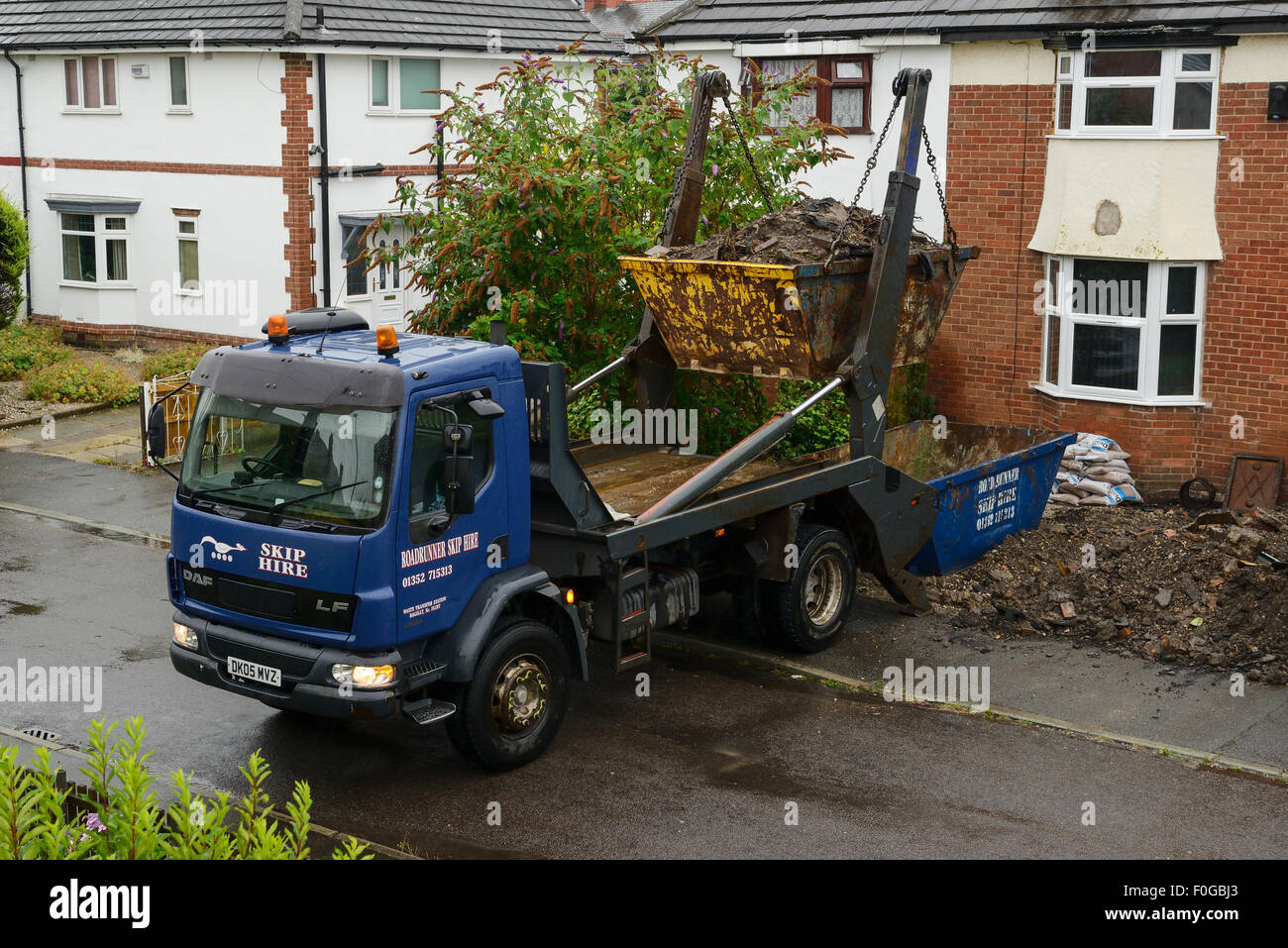 Vehicle collecting a skip from the front garden of a house Stock Photo