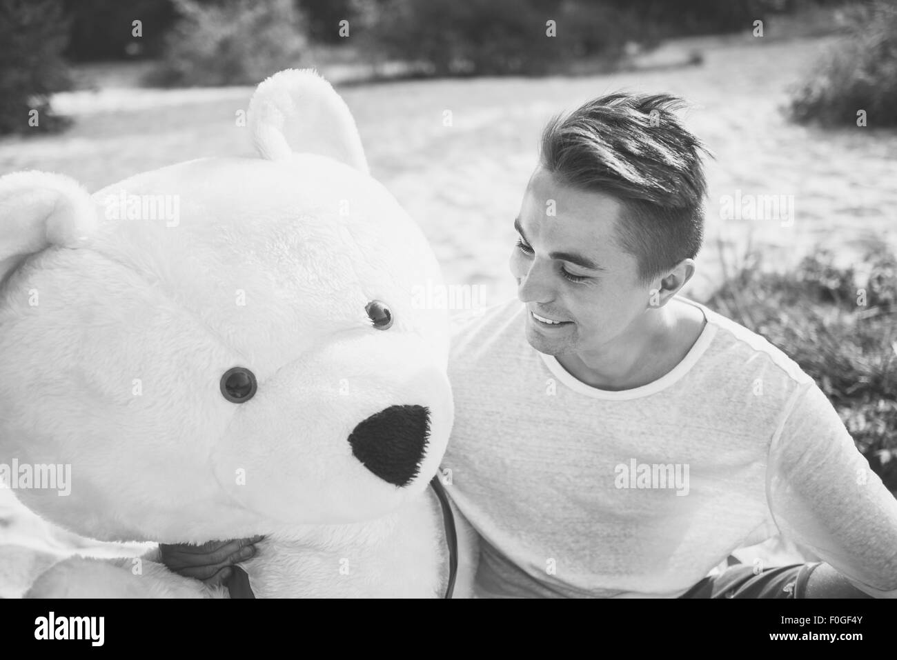 Handsome young man is fooling around with his massive teddy bear. Stock Photo