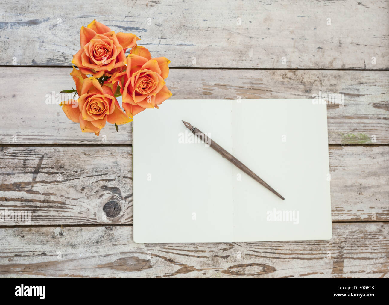 three orange roses on rustic wooden table with open notebook and pen Stock Photo