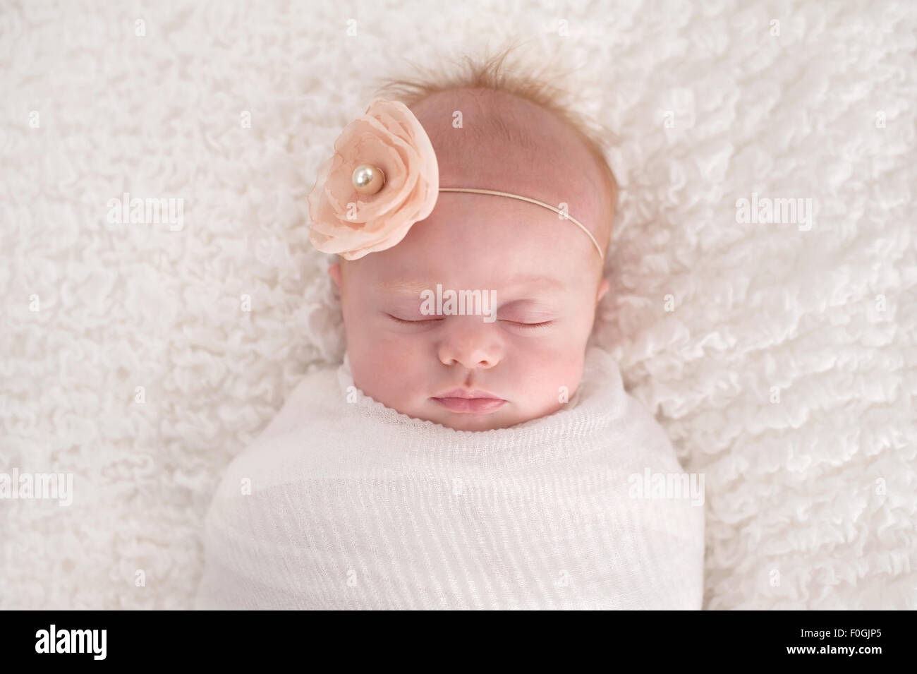 A seven week old baby girl swaddled in white and wearing a flower