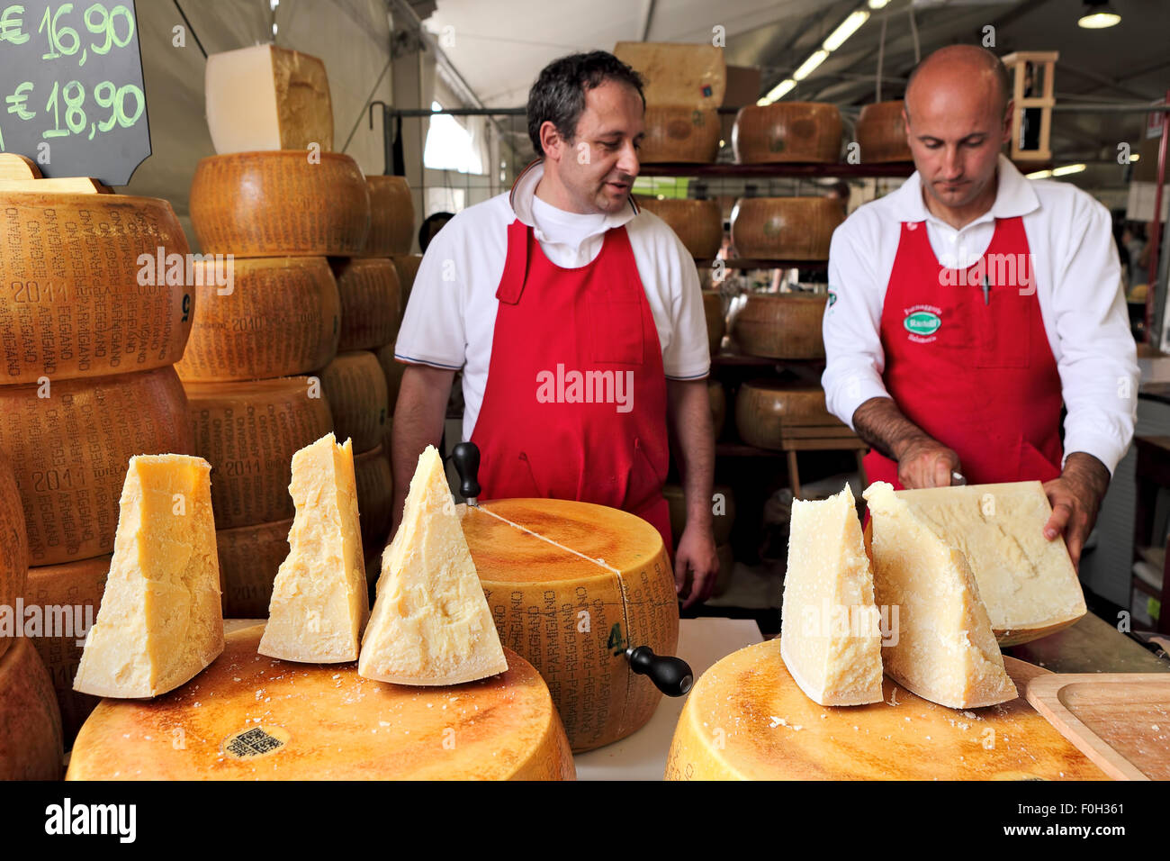 Two cheese makers and  stands with Parmesan - italian hard cheese made from raw cow's milk. Stock Photo