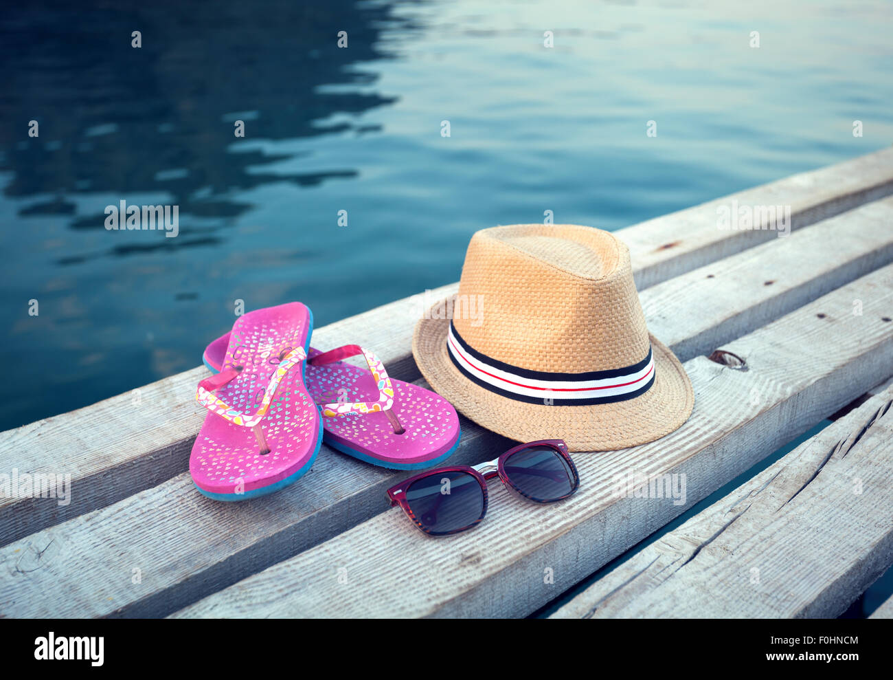 Sunglasses, flip-flops and hat on the wooden texture in summer. Stock Photo