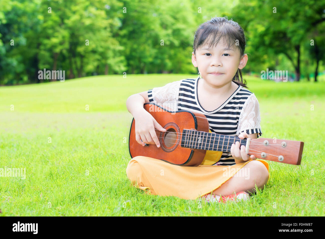 Asian kids sitting on grass and play ukulele in park Stock Photo