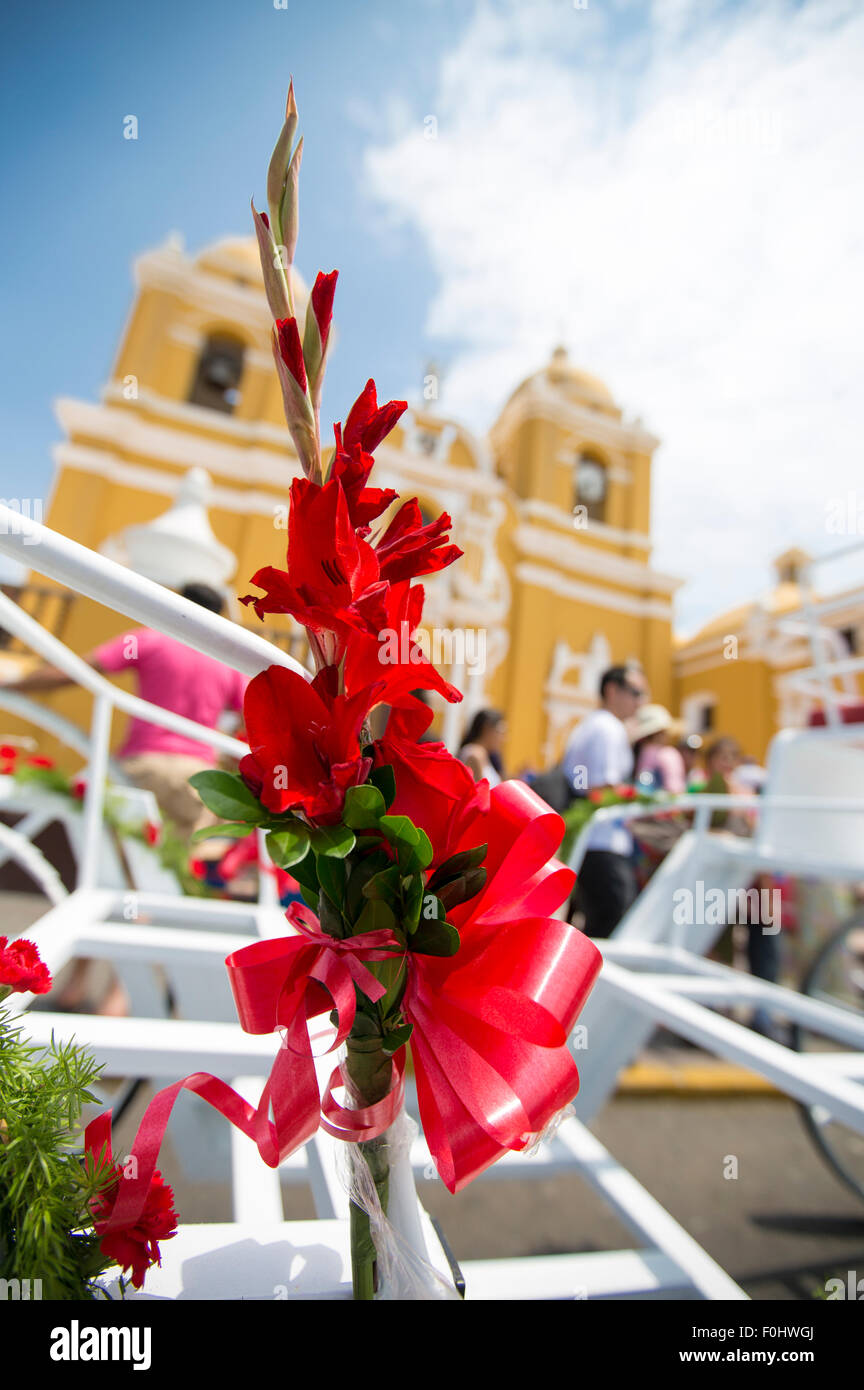 Red flowers attached to a horse carriage with the Church of Santo Domingo and people in the background. Trujillo - Peru Stock Photo