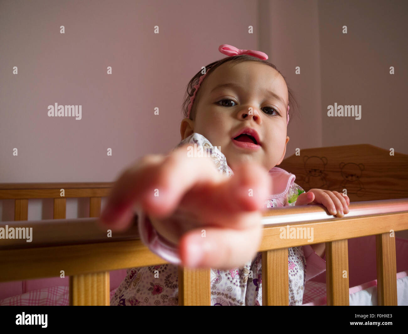 Baby girl inside crib pointing at camera Stock Photo