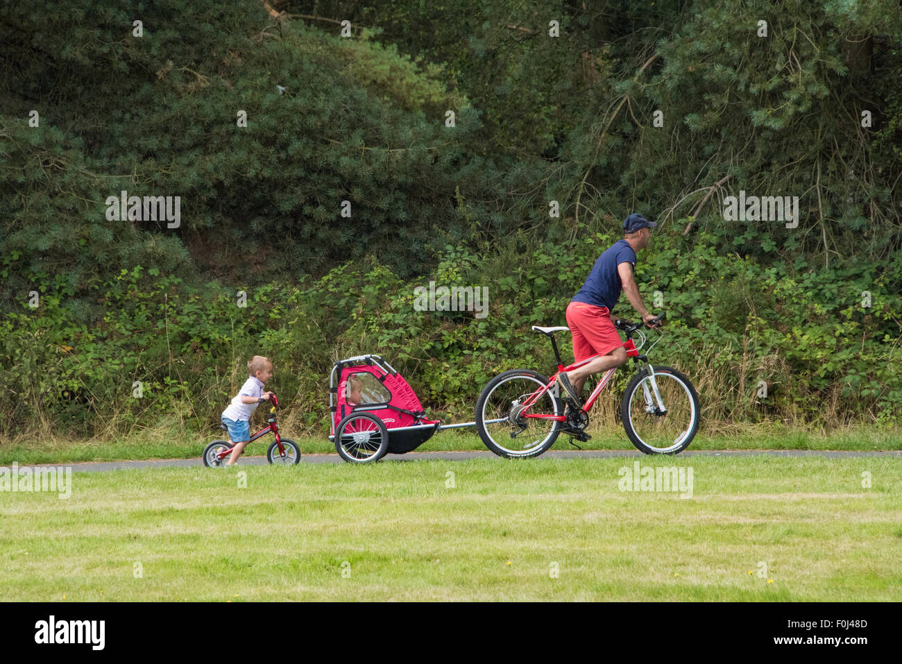 A man riding his bike with a child trailer and a young boy riding behind them at Cannock Chase Visitor Centre UK Stock Photo