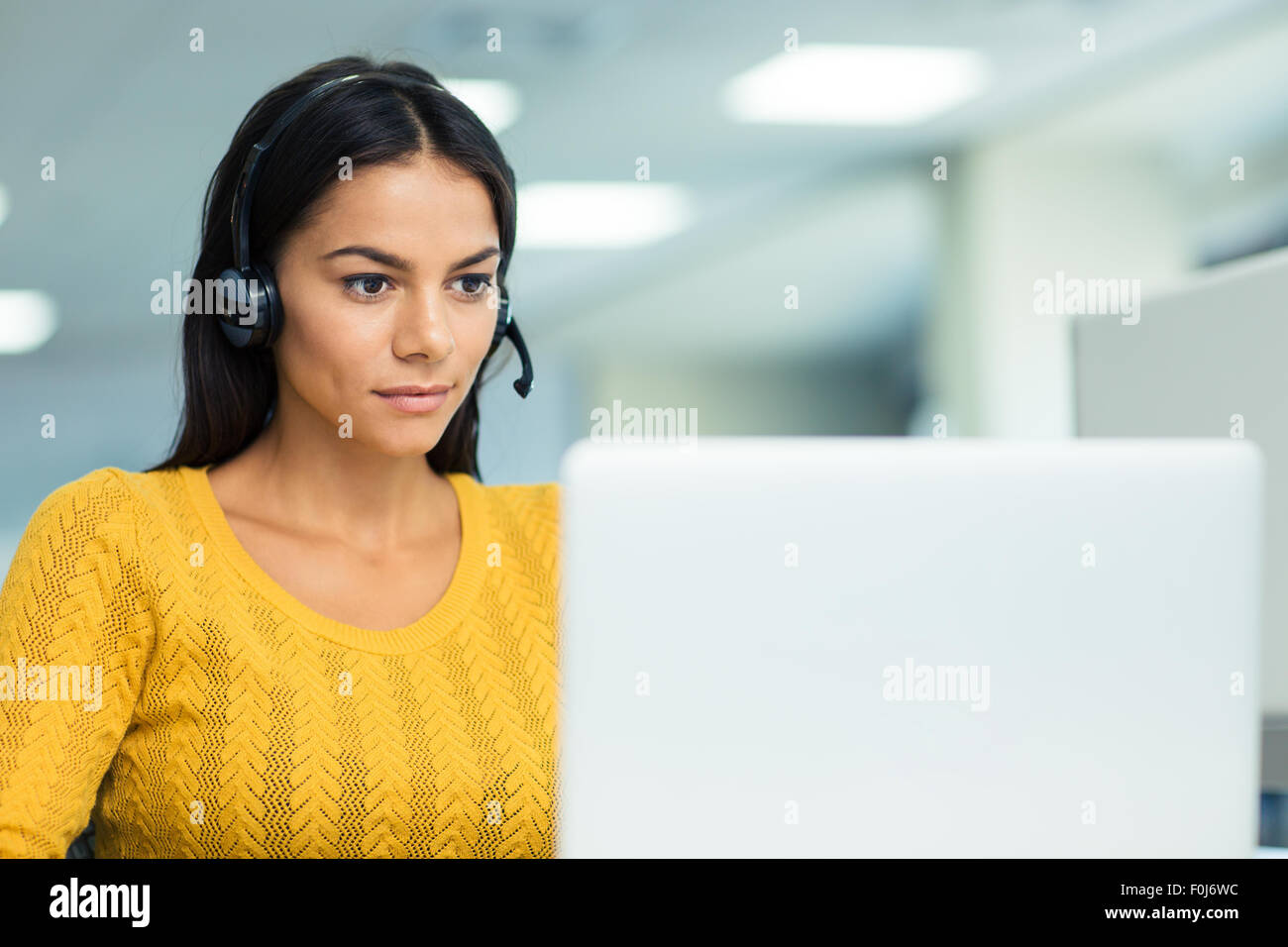 Portrait of a young businesswoman in headphones using laptop in office ...
