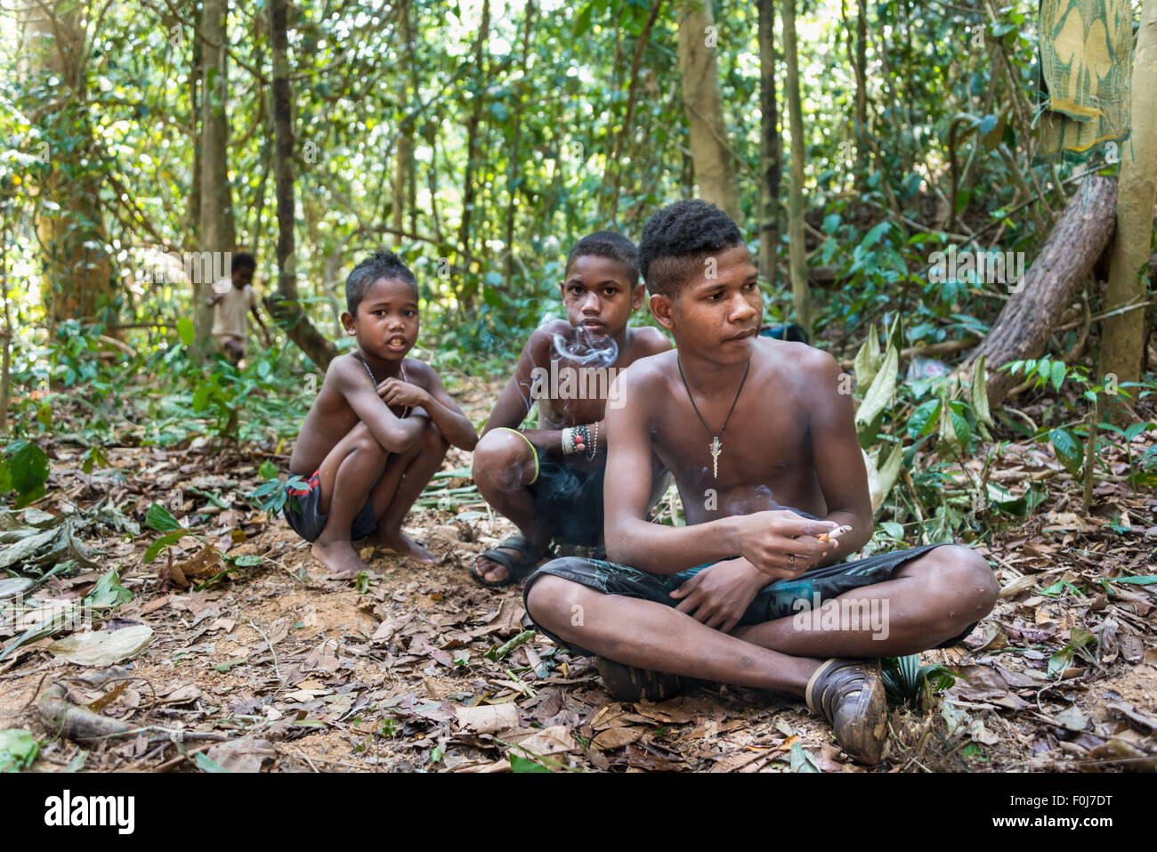 Three boys of the Orang Asil tribe sitting on the ground in the jungle and smoking, indigenous people, tropical rain forest Stock Photo