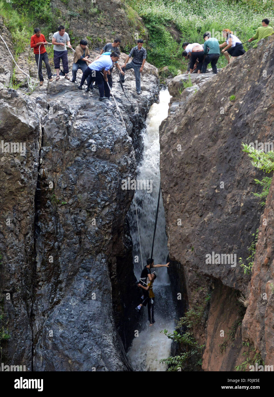 Weining, China's Guizhou Province. 16th Aug, 2015. People rescue a boy at Diaoshui Village of Mazha Town in Weining County, southwest China's Guizhou Province, Aug. 16, 2015. The boy was washed down the waterfall and hung between the cliffs on Sunday. © Yang Wenbin/Xinhua/Alamy Live News Stock Photo