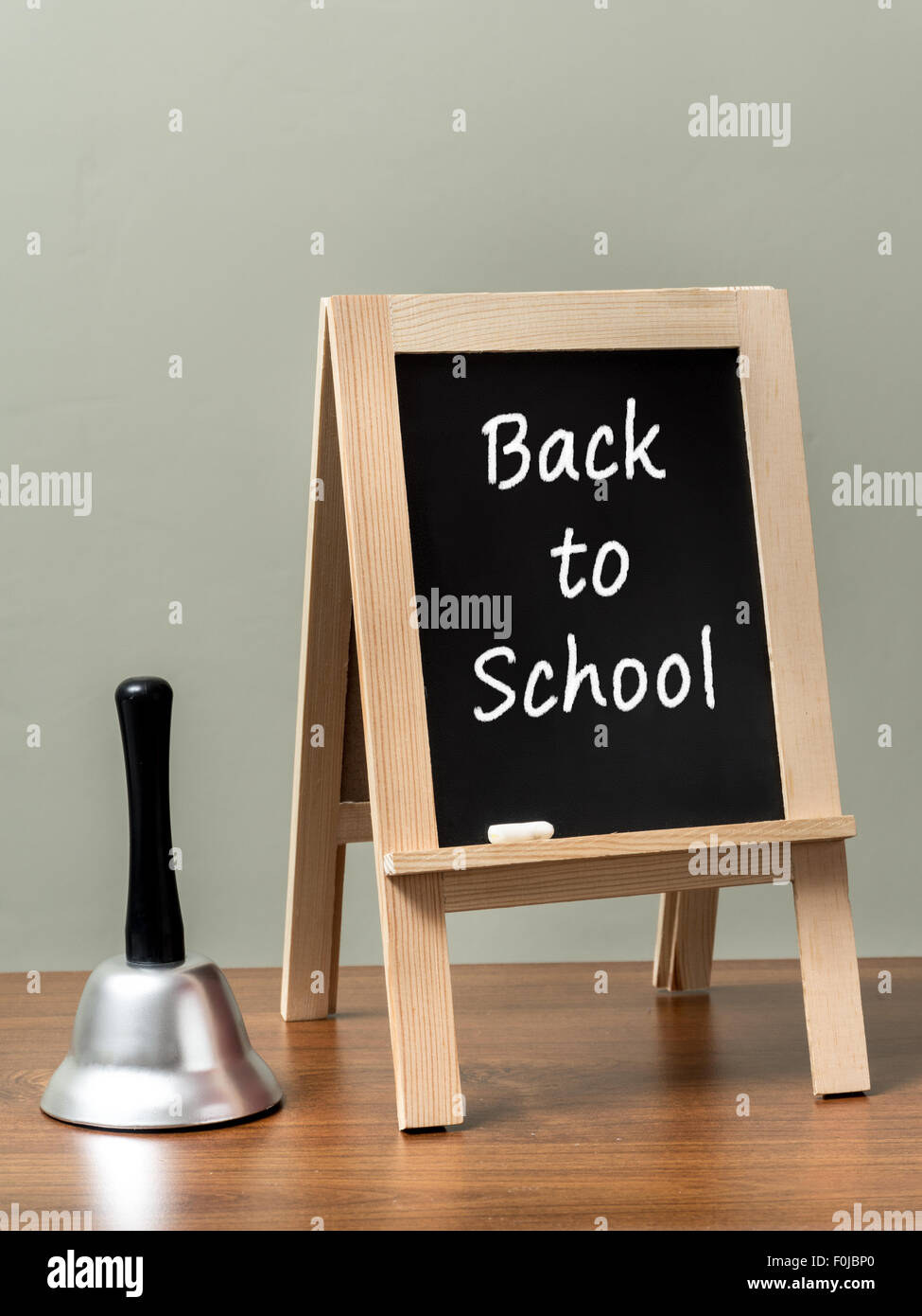 Silver handbell and blackboard with Back to School phrase placed on brown desktop over green wall Stock Photo