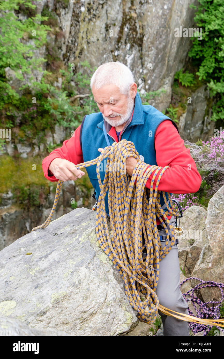 Experienced male rock climber unwrapping a climbing rope at top of a crag climb. North Wales, UK, Britain Stock Photo